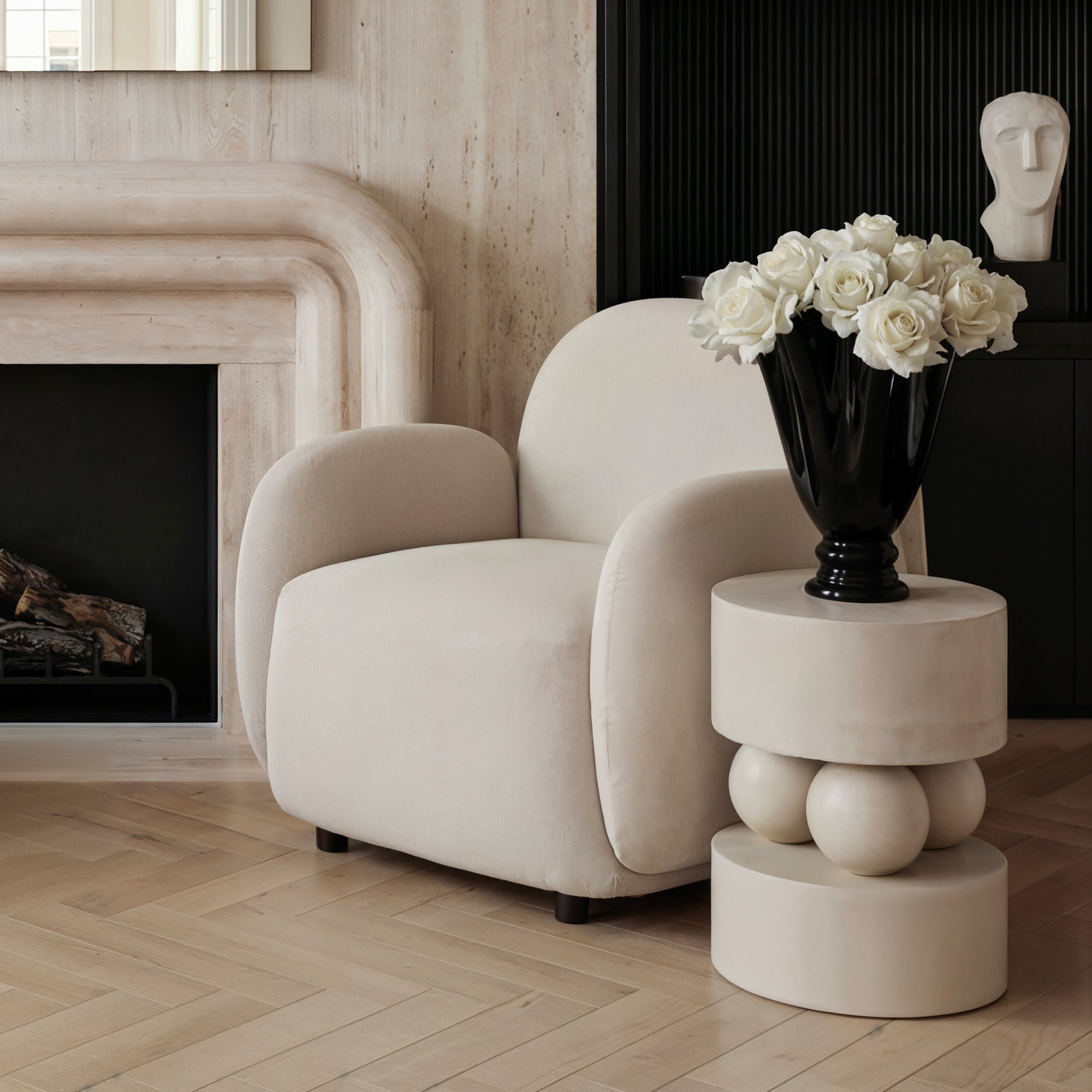 Modern living room with a beige armchair, marble side table, and black vase with white flowers.