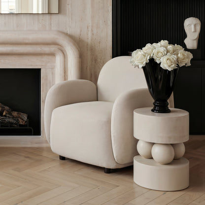 Modern living room with a beige armchair, marble side table, and black vase with white flowers.