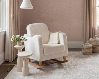 White rocking chair in a cozy room with a lamp and decorative items.
